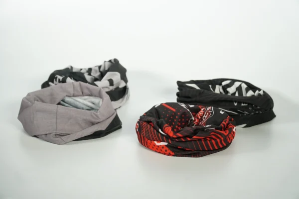 Four rolled promotional buffs with branded prints side by side – Textile Promos