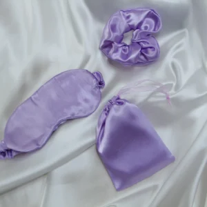 Lavender satin sleep set with eye mask, scrunchie, and pouch on white satin fabric background